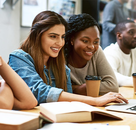 Women, students in library with laptop and studying for exam on pc and learning on university campus
